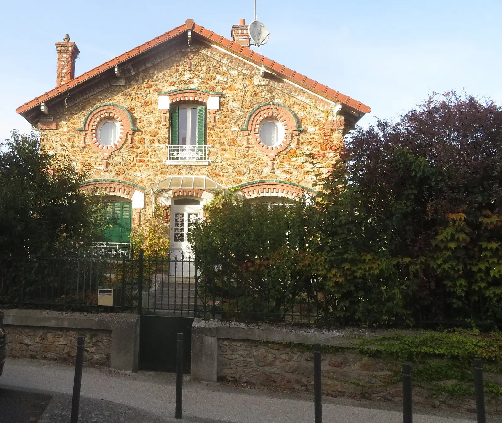 Pavillon francilien en pierre meulière avec encadrements de brique, derrière un muret