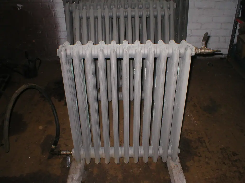 Ancien radiateur en fonte à colonnes, repeint en blanc, raccordé à un réseau d’eau chaude